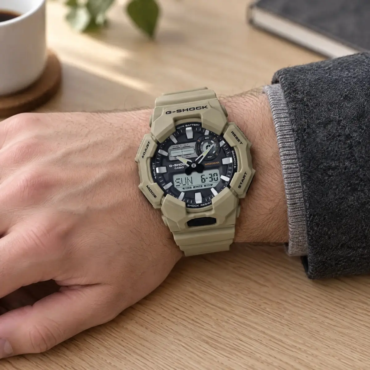 Casio G-SHOCK homokszínű karóra férfi csuklón, világos fa asztallapon