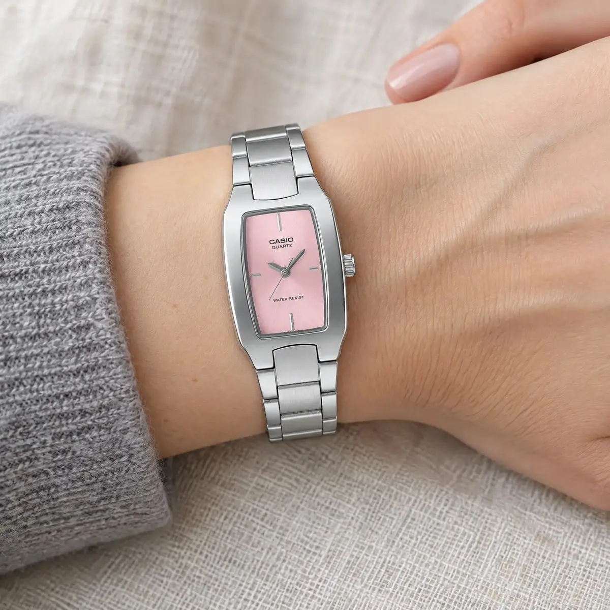 Casio hordó alakú karóra rózsaszín számlappal és acél szíjjal, női csuklón, világos vászonszöveten