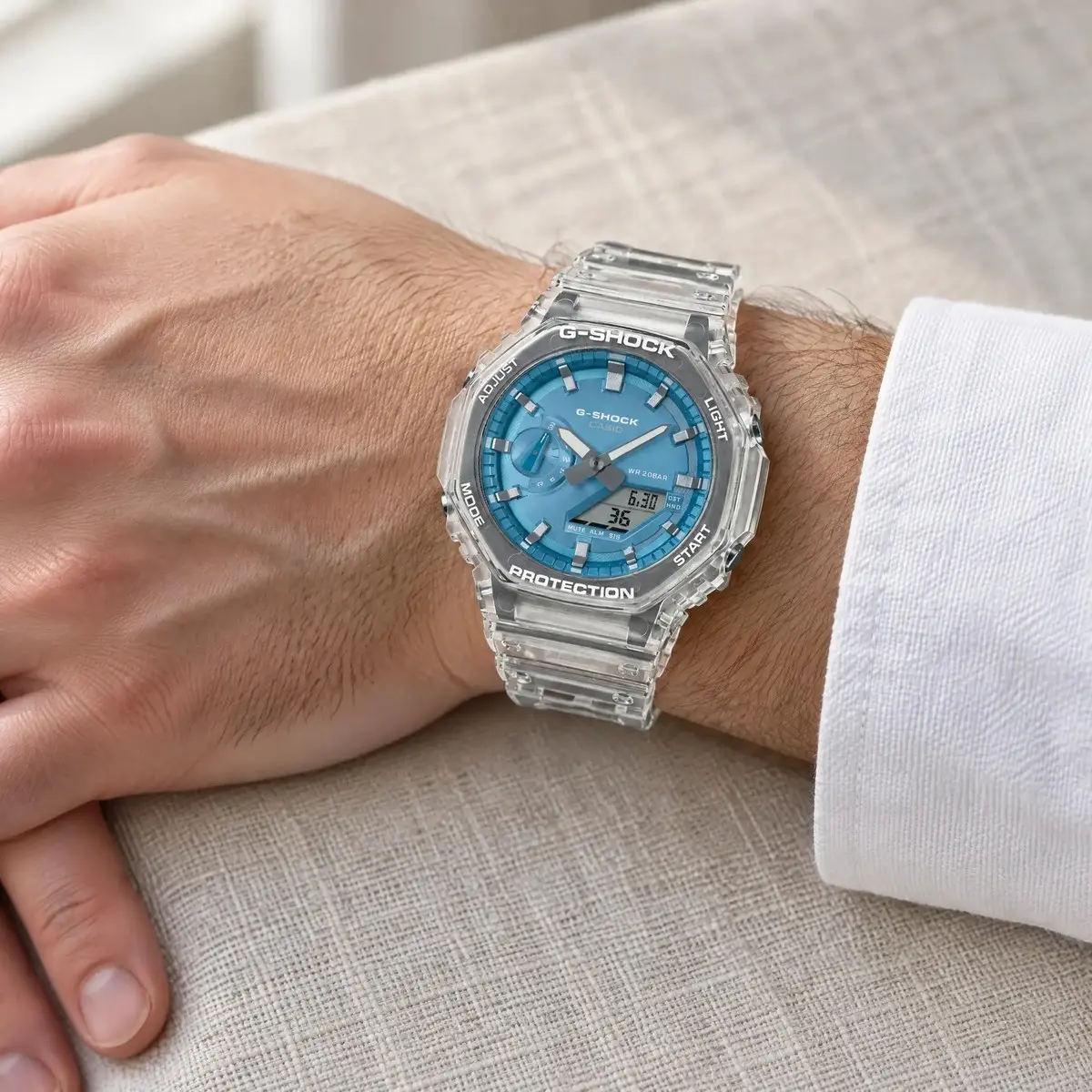 Casio G-Shock átlátszó óra kék számlappal, férfi csuklón, fehér ing mandzsettája mellett