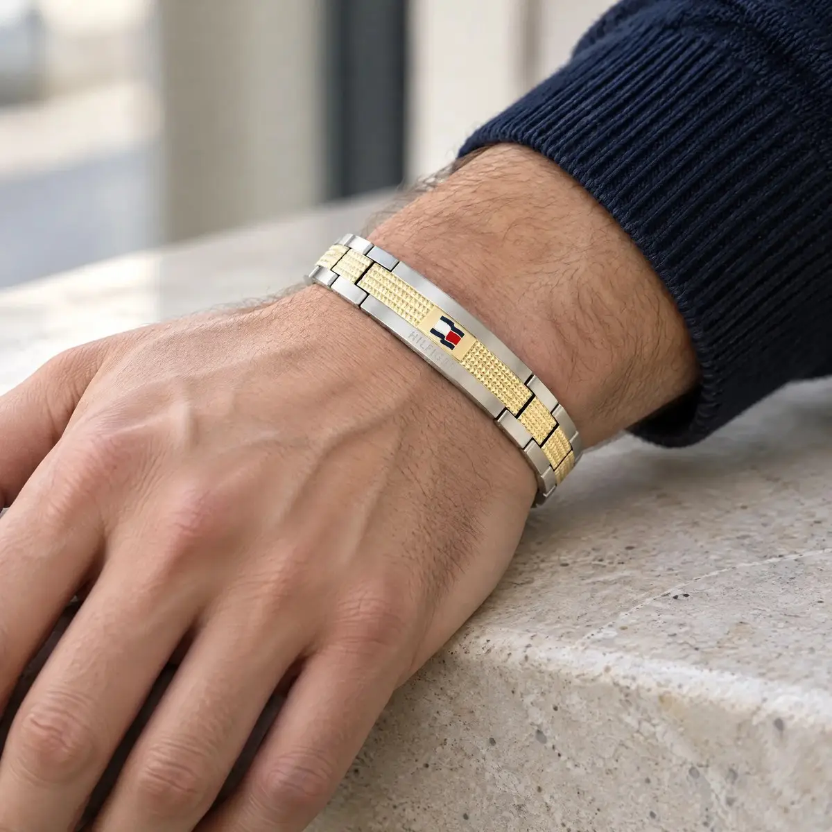 Tommy Hilfiger acél karkötő arany színű betétekkel és zászlós logóval, férfi csuklón, kőlap szélén