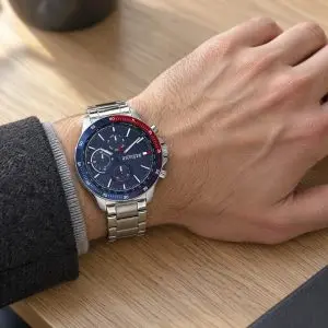 Tommy Hilfiger acél karóra kék számlappal, kék és piros lünettával, férfi csuklón, fa asztalon