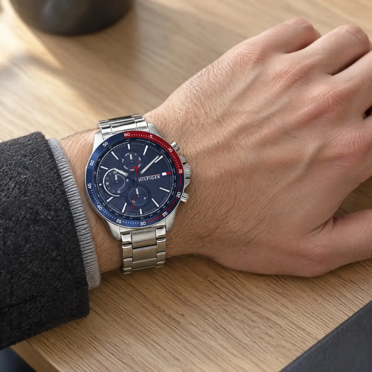 Tommy Hilfiger acél karóra kék számlappal, kék és piros lünettával, férfi csuklón, fa asztalon